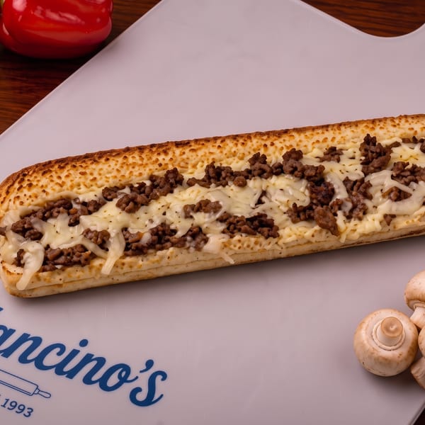 A cheesesteak grinder with steak and melted cheese on a Mancino's board.