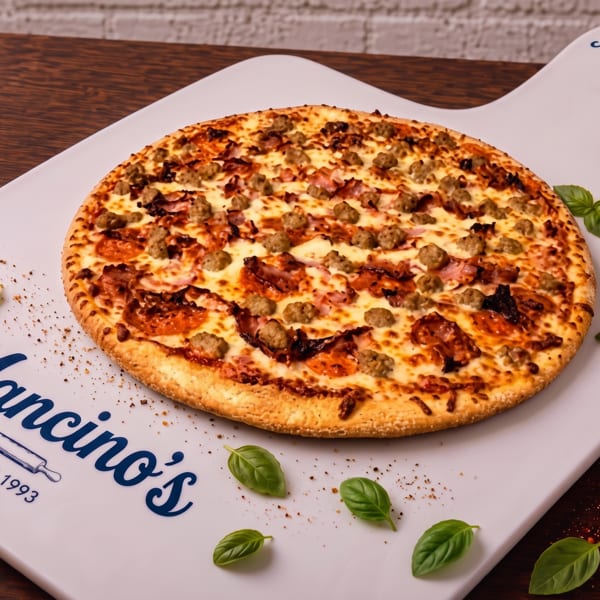 Mano’s pizza topped with pepperoni, sausage, bacon, and melted cheese on a branded serving board with basil leaves.