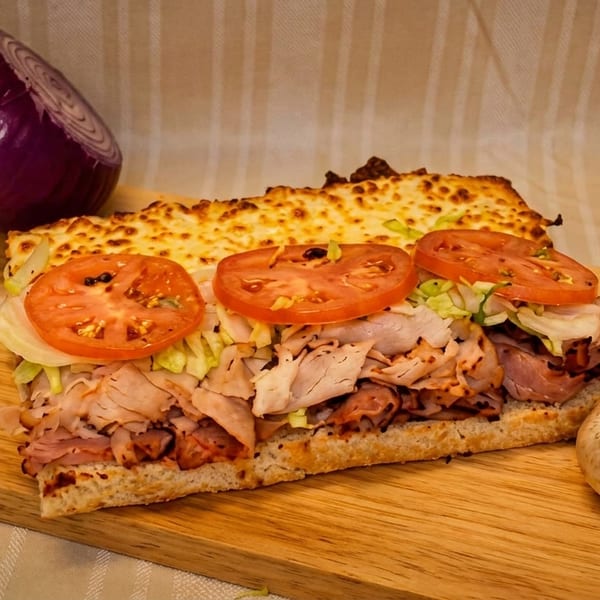 A toasted sub sandwich with melted cheese, turkey, ham, lettuce, and tomatoes on a wooden board.