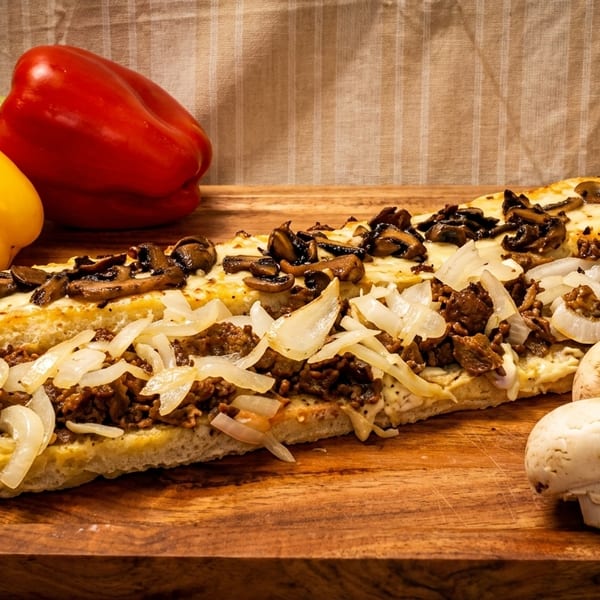 Cheesesteak sandwich on a wooden board with bell peppers and mushrooms.