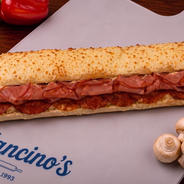 A ham and pepperoni combo grinder with melted cheese on a Mancino's board.