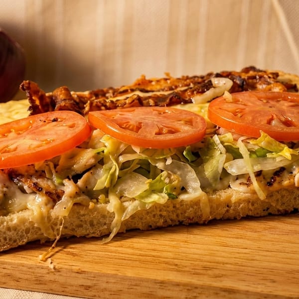 A chicken sub sandwich with melted cheese, lettuce, and tomato slices on a wooden board.